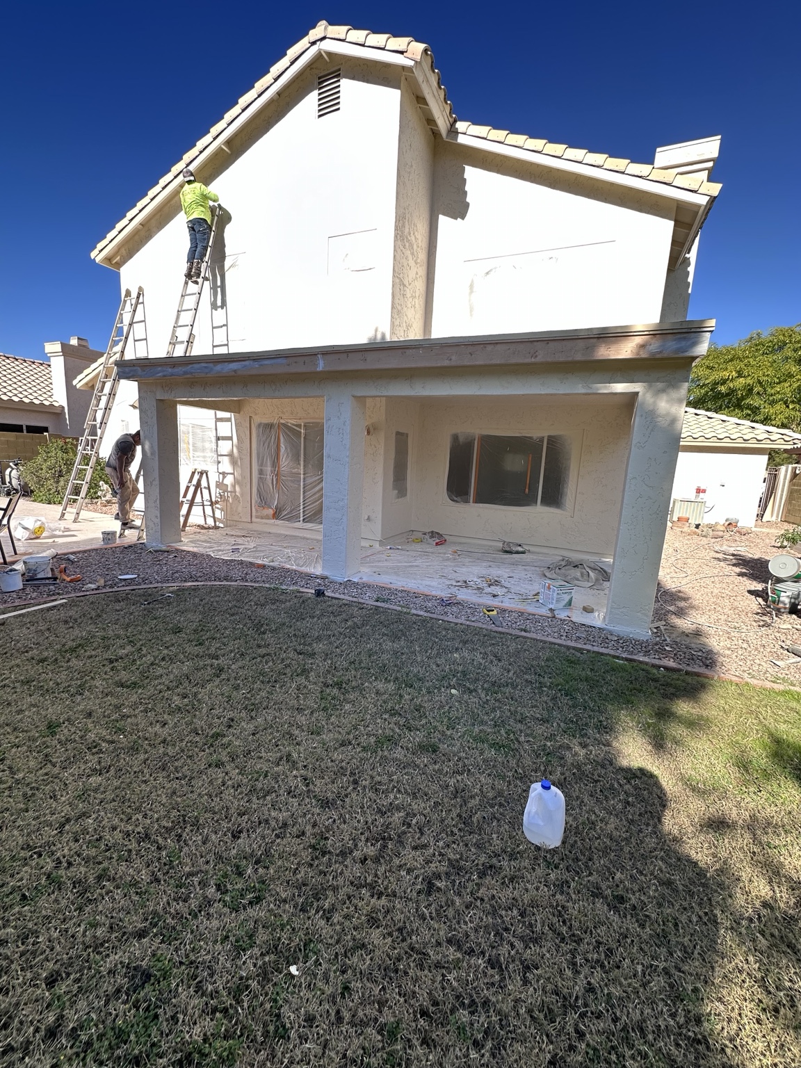 Two-story stucco home masked and prepared for professional exterior painting